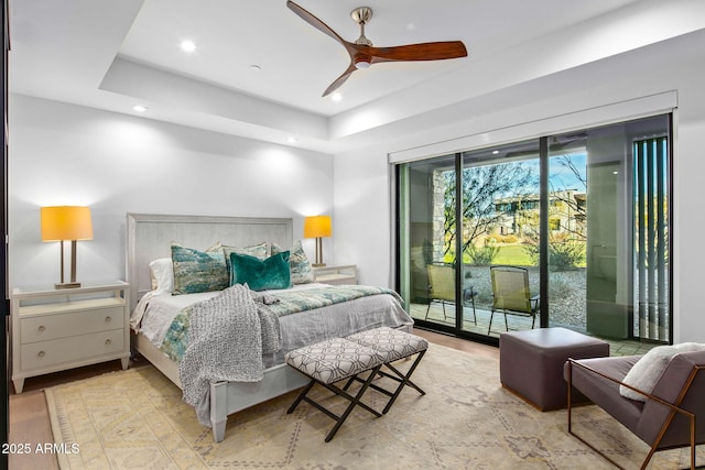 bedroom featuring access to exterior, a tray ceiling, ceiling fan, and light wood-type flooring