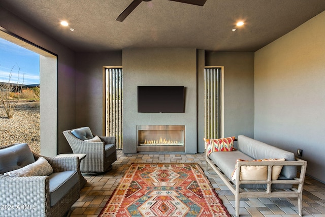 interior space with ceiling fan, a textured ceiling, and an outdoor fireplace