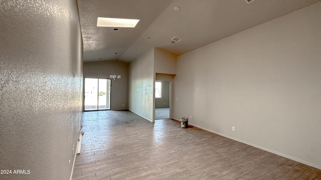 spare room featuring light wood-type flooring, an inviting chandelier, and lofted ceiling with skylight