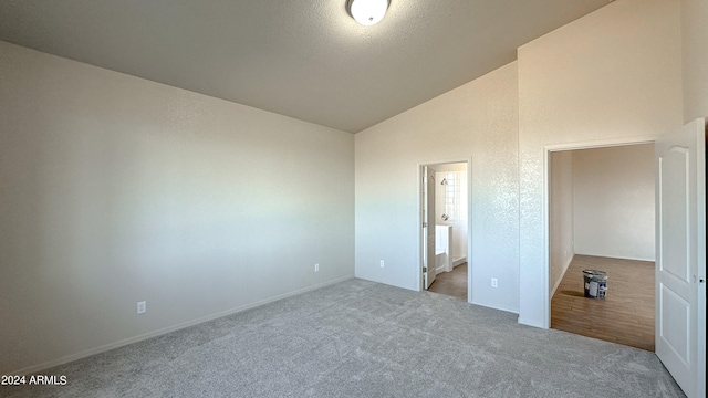 unfurnished bedroom featuring ensuite bathroom, light colored carpet, a textured ceiling, and vaulted ceiling