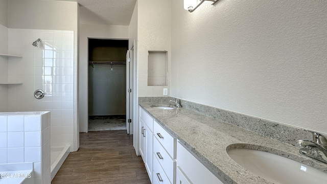 bathroom with hardwood / wood-style floors, vanity, a tile shower, and a textured ceiling