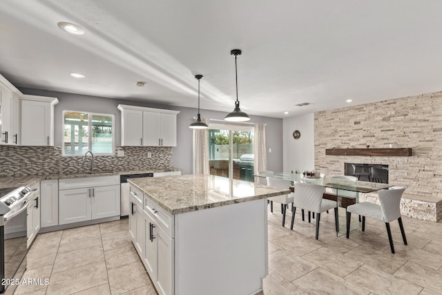 kitchen featuring backsplash, a kitchen island, light stone countertops, appliances with stainless steel finishes, and a sink