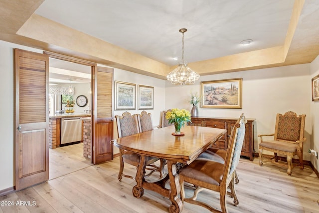 dining room with a tray ceiling, light hardwood / wood-style floors, and a notable chandelier