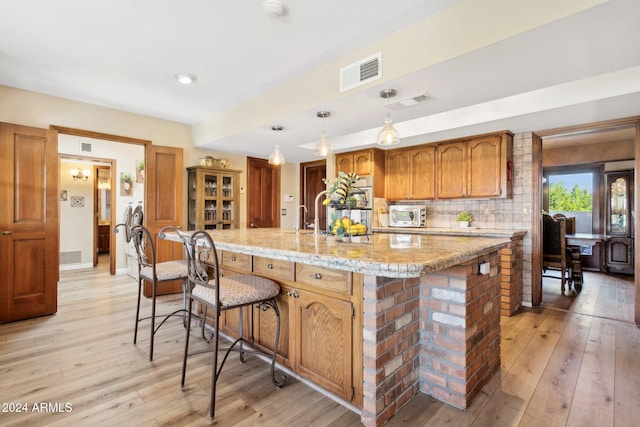 kitchen featuring an island with sink, pendant lighting, and light wood-type flooring