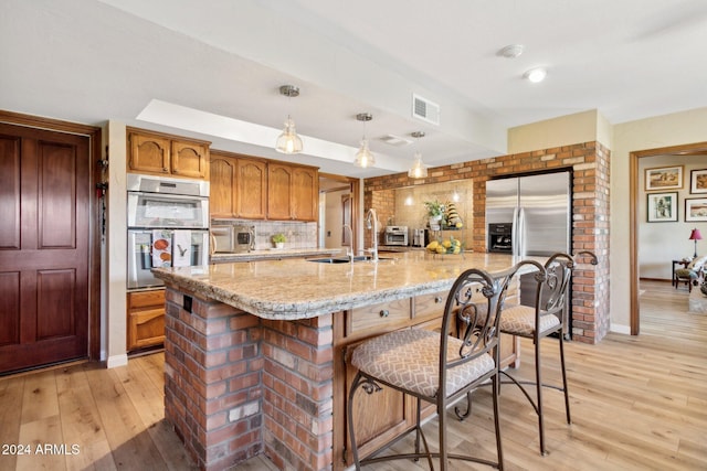 kitchen featuring decorative light fixtures, sink, light wood-type flooring, and stainless steel appliances