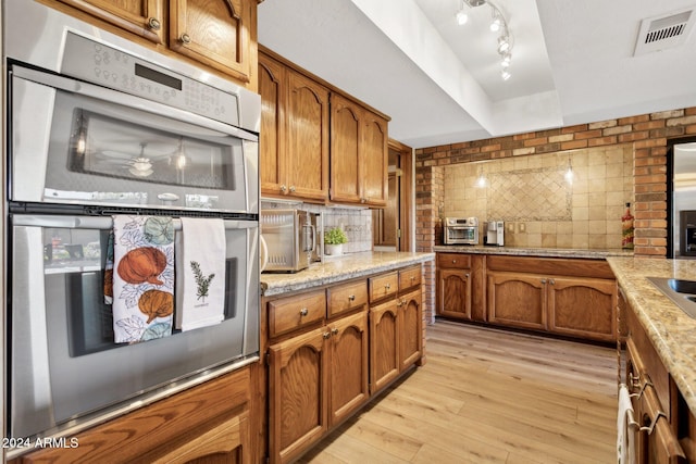 kitchen with light stone countertops, light wood-type flooring, tasteful backsplash, and double oven