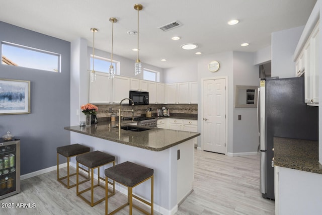 kitchen with sink, stainless steel fridge, hanging light fixtures, wine cooler, and kitchen peninsula