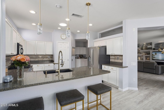 kitchen with pendant lighting, sink, dark stone countertops, white cabinets, and stainless steel fridge with ice dispenser