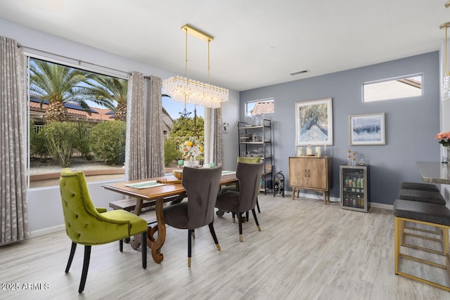 dining area with a notable chandelier, plenty of natural light, beverage cooler, and light wood-type flooring