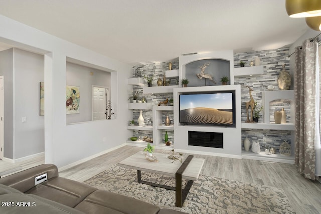 living room featuring built in shelves, a fireplace, and light wood-type flooring