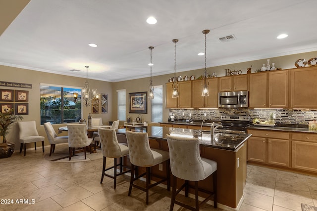 kitchen with a kitchen bar, stainless steel appliances, a center island with sink, hanging light fixtures, and crown molding