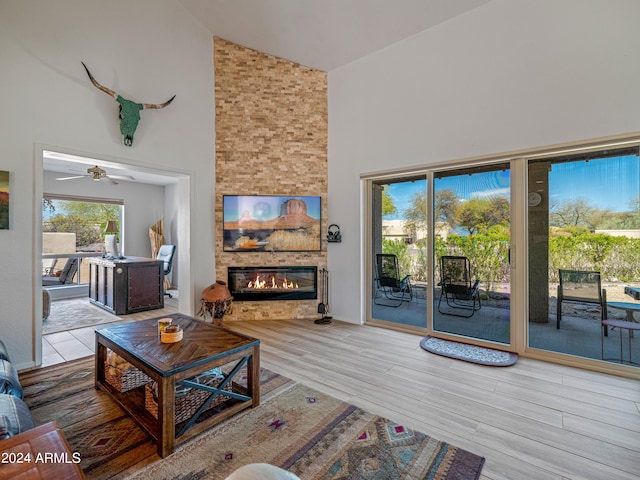 living room featuring light hardwood / wood-style flooring, high vaulted ceiling, ceiling fan, and a stone fireplace