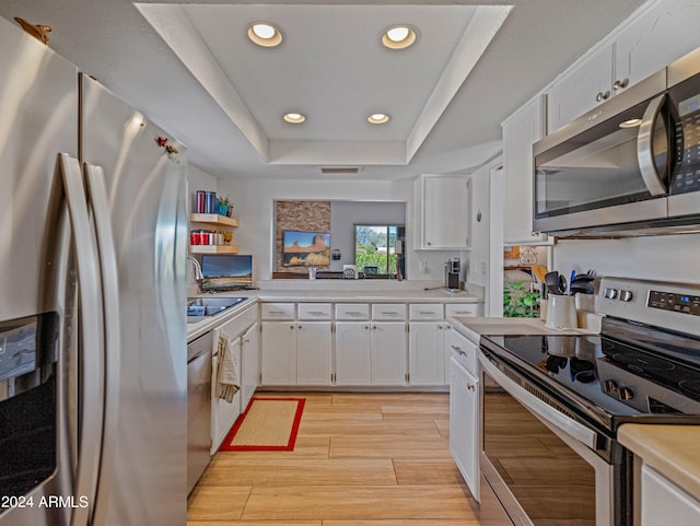 kitchen featuring a raised ceiling, light hardwood / wood-style floors, white cabinets, and appliances with stainless steel finishes