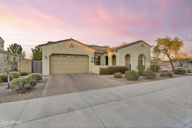 mediterranean / spanish-style home featuring an attached garage, fence, a tile roof, decorative driveway, and stucco siding