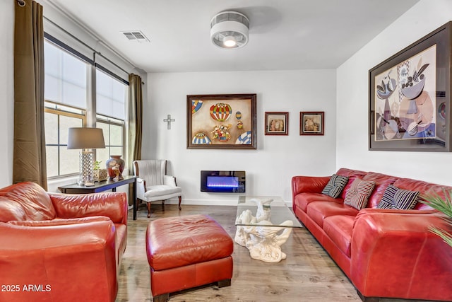 living area featuring a glass covered fireplace, visible vents, and wood finished floors