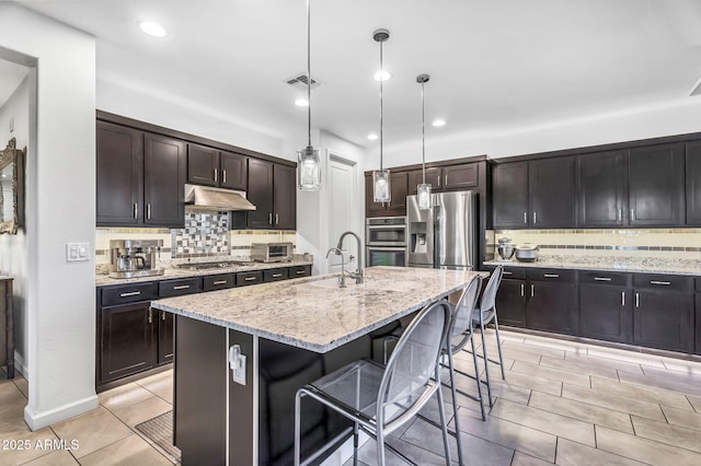 kitchen featuring stainless steel appliances, visible vents, a sink, under cabinet range hood, and a kitchen bar