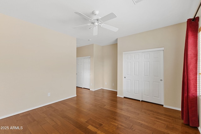 unfurnished bedroom with multiple closets, ceiling fan, baseboards, and dark wood-type flooring