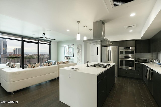 kitchen with ceiling fan, a kitchen island with sink, decorative light fixtures, island range hood, and appliances with stainless steel finishes