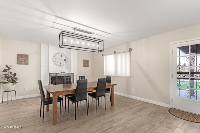 dining area featuring a brick fireplace, a notable chandelier, and light wood-type flooring