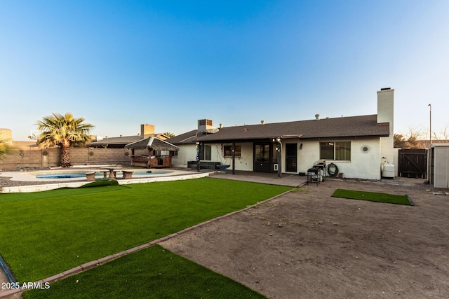 back house at dusk featuring a yard, a pool with hot tub, and a patio