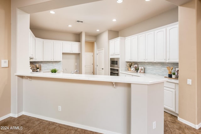 kitchen with light tile patterned flooring, kitchen peninsula, white cabinets, stainless steel appliances, and backsplash