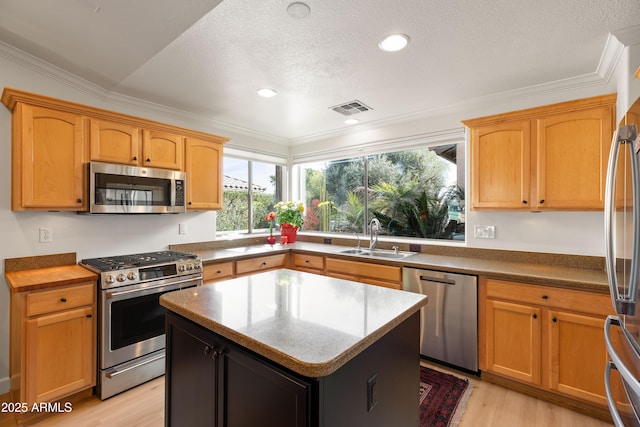 kitchen with a kitchen island, appliances with stainless steel finishes, sink, crown molding, and light wood-type flooring