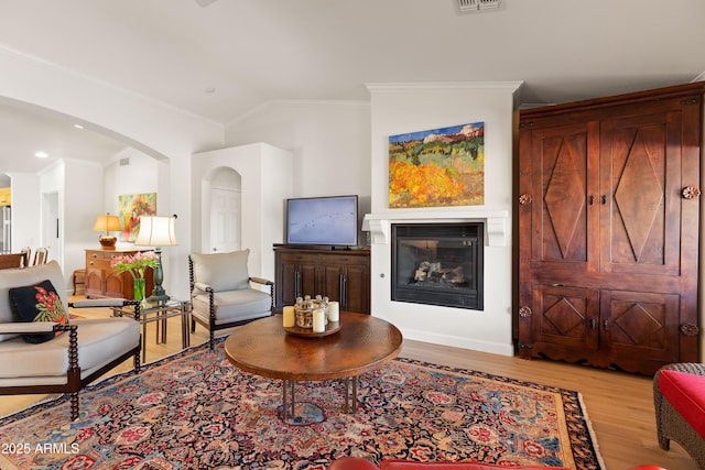 living room featuring vaulted ceiling, ornamental molding, and light wood-type flooring