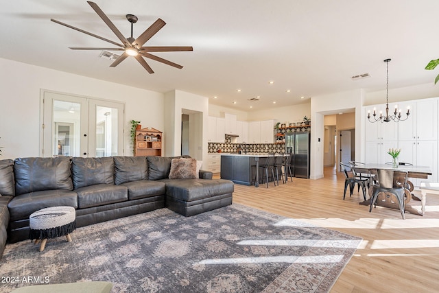 living room featuring french doors, light wood-type flooring, and ceiling fan with notable chandelier