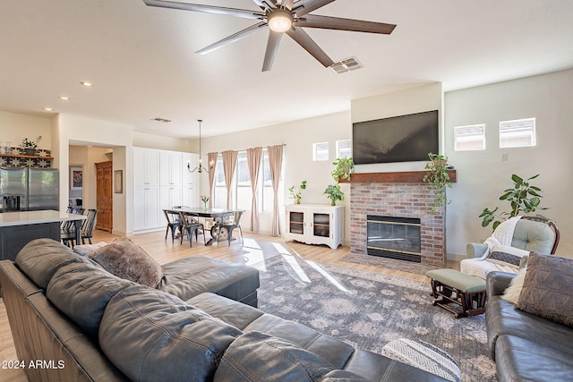 living room featuring light hardwood / wood-style floors, ceiling fan with notable chandelier, and a brick fireplace