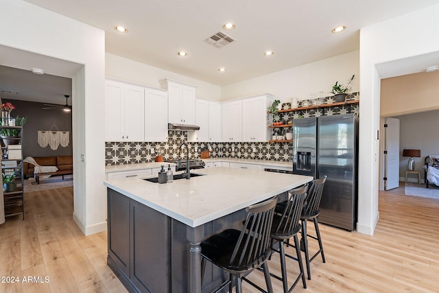 kitchen featuring backsplash, a center island with sink, stainless steel fridge with ice dispenser, light wood-type flooring, and white cabinets