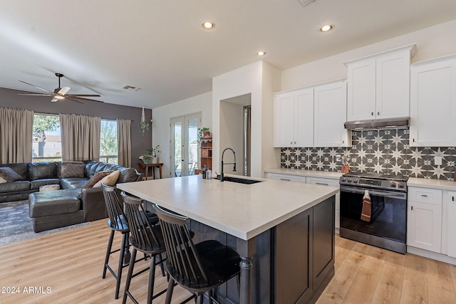 kitchen with sink, stainless steel range, a kitchen island with sink, and white cabinets