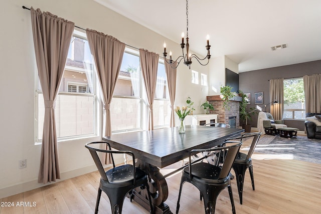 dining area featuring a notable chandelier, light wood-type flooring, and a brick fireplace