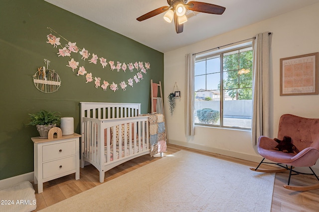 bedroom featuring a crib, light hardwood / wood-style floors, and ceiling fan