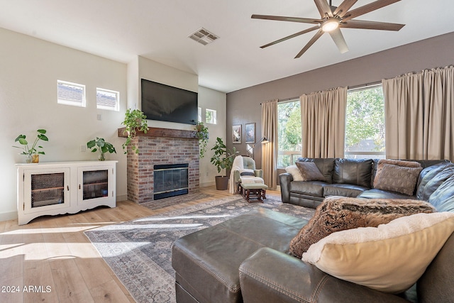 living room with a brick fireplace, light wood-type flooring, and ceiling fan