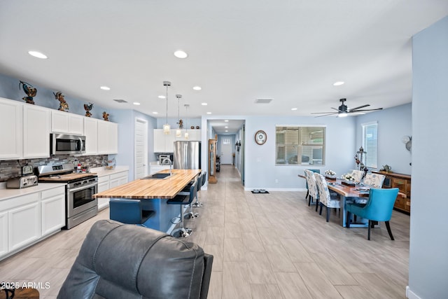 kitchen featuring appliances with stainless steel finishes, white cabinetry, pendant lighting, and an island with sink