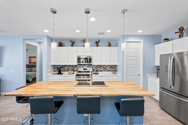 kitchen featuring decorative light fixtures, white cabinetry, an island with sink, and appliances with stainless steel finishes