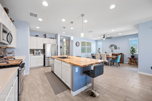 kitchen featuring wood counters, a center island with sink, white cabinets, and stainless steel appliances