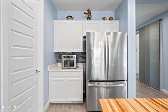 kitchen with backsplash, stainless steel refrigerator, white cabinetry, and light hardwood / wood-style flooring