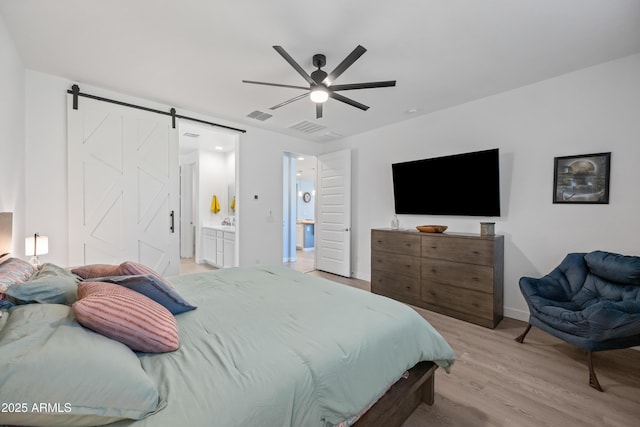 bedroom featuring ceiling fan, a barn door, light wood-type flooring, and connected bathroom