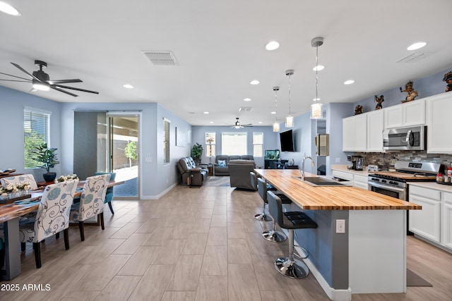 kitchen with stainless steel appliances, sink, butcher block countertops, white cabinetry, and an island with sink