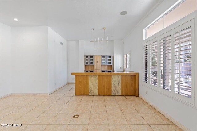 kitchen with hanging light fixtures, light tile patterned floors, sink, ornamental molding, and kitchen peninsula