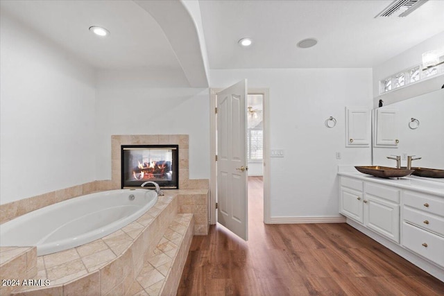 bathroom featuring vanity, a tiled fireplace, hardwood / wood-style flooring, and a relaxing tiled tub