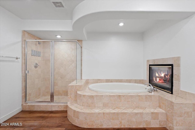 bathroom featuring a stall shower, a garden tub, visible vents, a fireplace, and wood finished floors