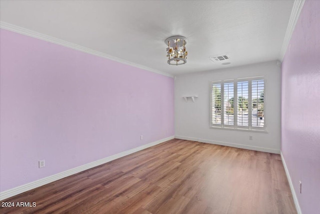 unfurnished room featuring a notable chandelier, ornamental molding, and hardwood / wood-style flooring