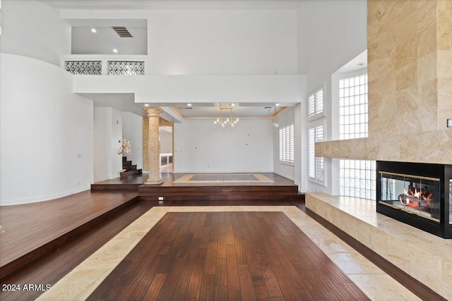 unfurnished living room featuring wood-type flooring, a high ceiling, and a high end fireplace