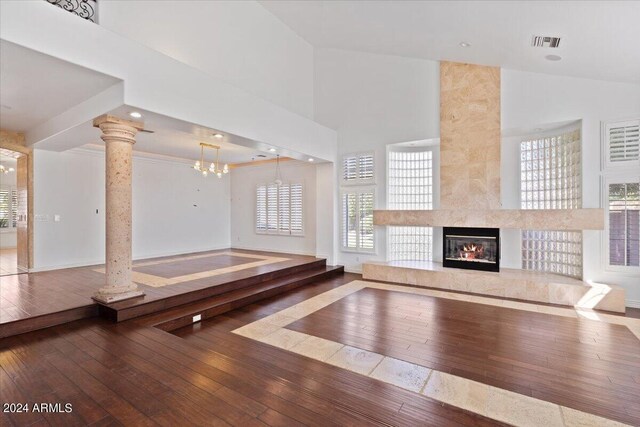 unfurnished living room featuring high vaulted ceiling, ornate columns, wood-type flooring, a chandelier, and a premium fireplace