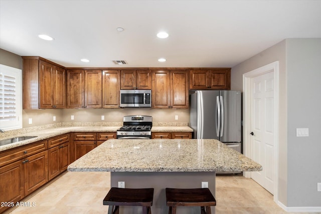 kitchen featuring a kitchen breakfast bar, appliances with stainless steel finishes, sink, light stone countertops, and a kitchen island