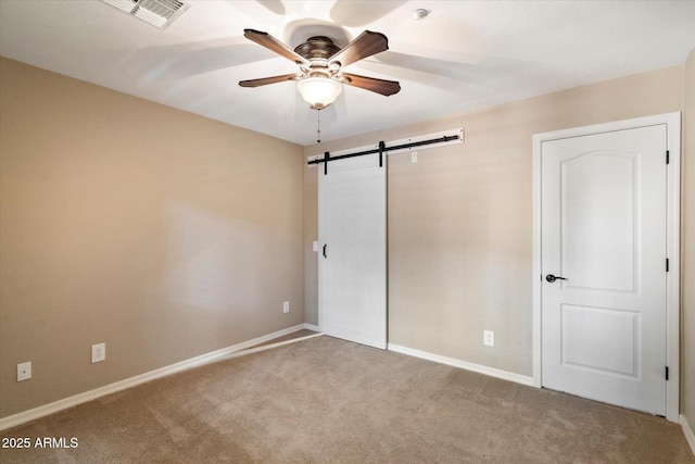 unfurnished bedroom featuring ceiling fan, light colored carpet, and a barn door