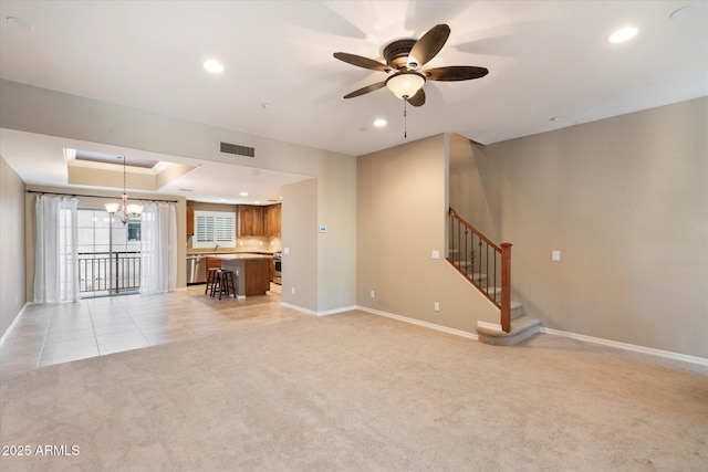 unfurnished living room featuring ceiling fan with notable chandelier, a raised ceiling, and light carpet