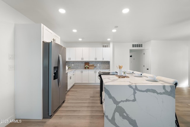 kitchen featuring stainless steel fridge, white cabinetry, a center island, light stone counters, and light wood-type flooring